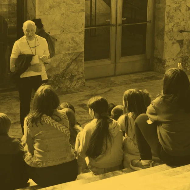 Man giving a lecture to a group of children on some steps outdoors.
