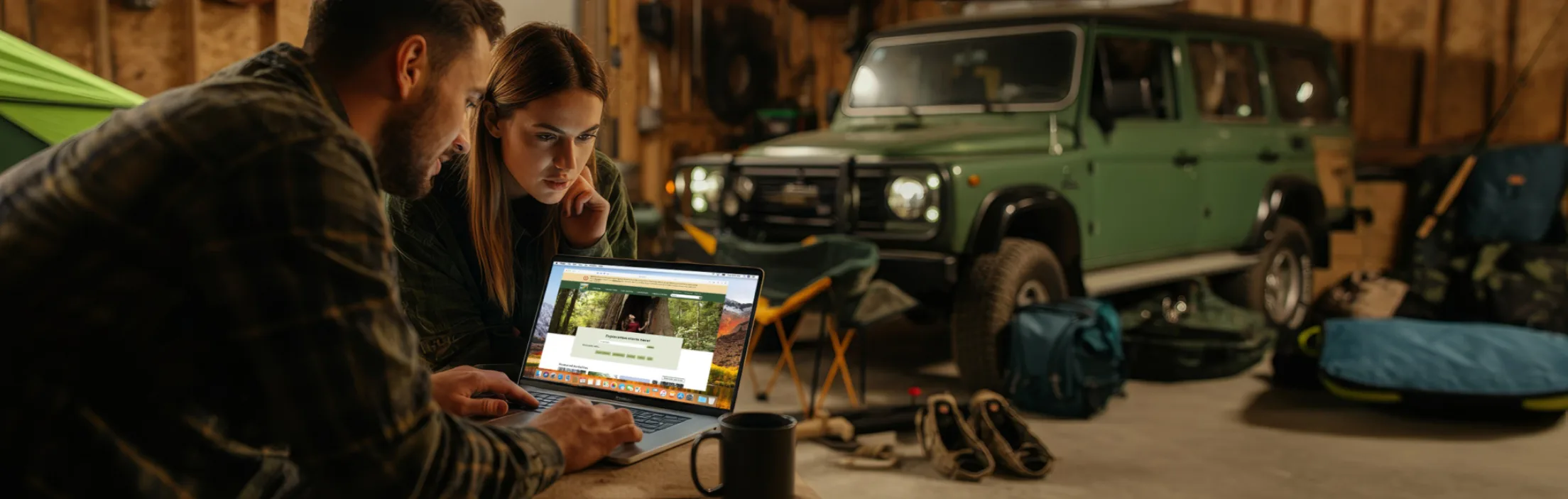 A young couple looking at a laptop showing the Washington State Parks website. An SUV and camping gear can be seen in the background.